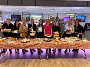 A picture of many bakers holding their plates and donation bucket during their coffee morning