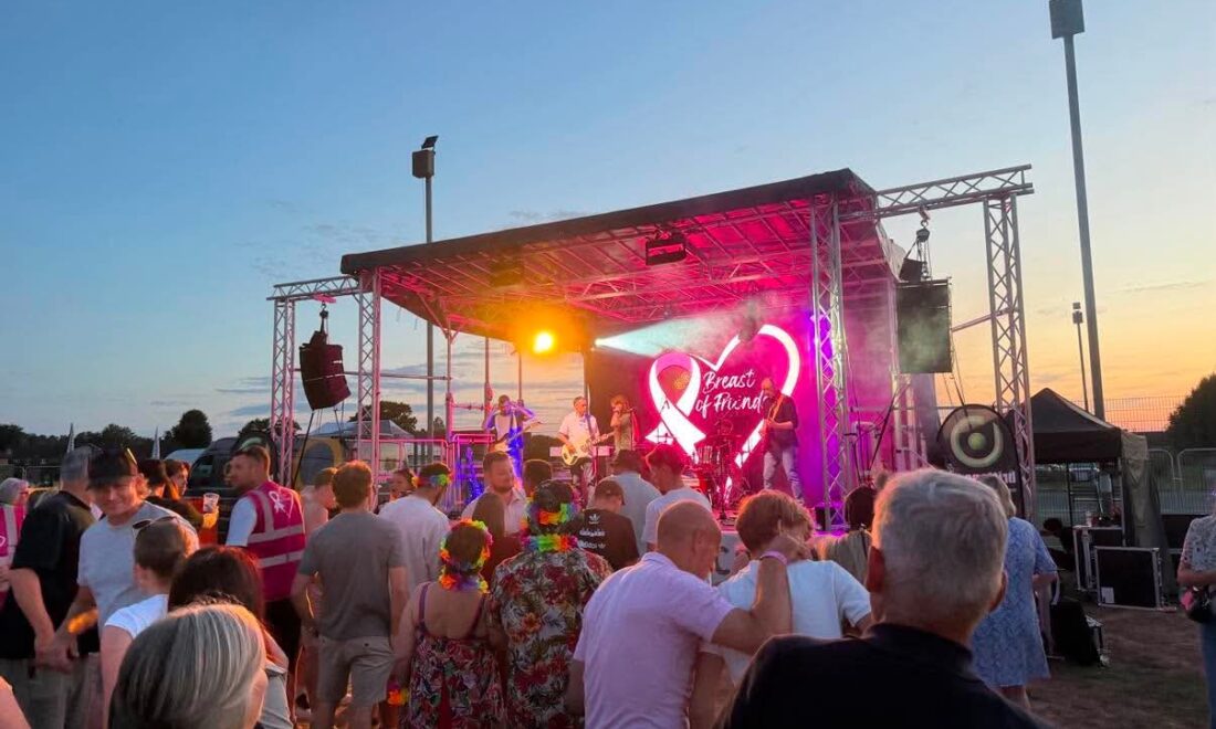 A photo of the stage at night with neon "Breast of Friends" charity logo in the background