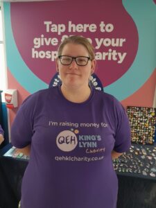 A photo of Maggie Drew smiling in front of a stall wearing a "I'm raising money for The QEHKL Charity" t shirt